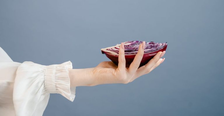 A woman's hand gracefully holds a sliced red cabbage against a blue background, symbolizing freshness and health.