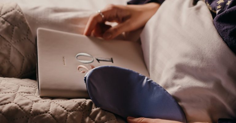 Close-up of a person holding a journal with a sleep mask on the bed, perfect for cozy nighttime routines.