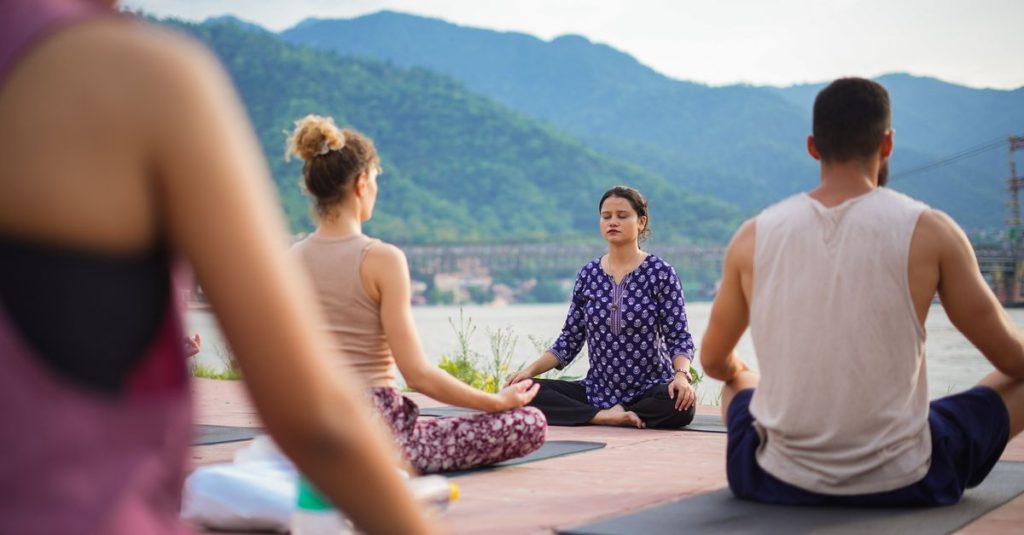 A group practicing yoga outdoors by the Ganges River in Rishikesh, India.