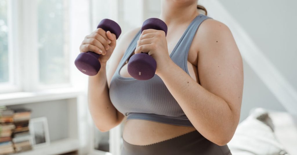 Plus size woman in activewear working out with dumbbells indoors, promoting body positivity.