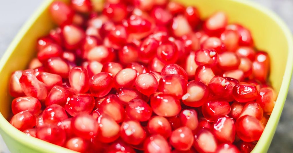 Vibrant red pomegranate seeds in a yellow bowl, highlighting natural freshness and health benefits.