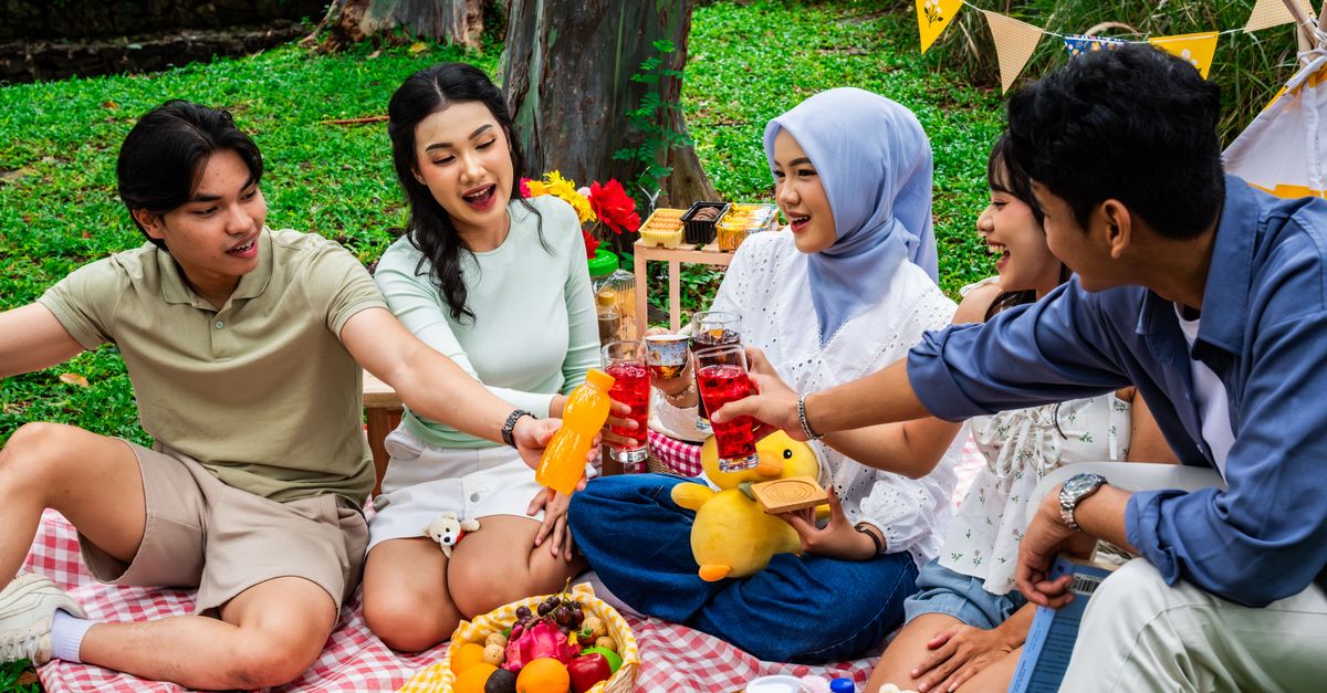 A group of friends enjoying a colorful picnic outdoors in Indonesia, celebrating friendship with snacks and drinks.
