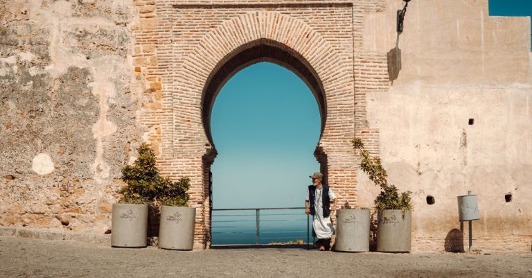 Person standing near an ancient Moroccan archway overlooking the sea.