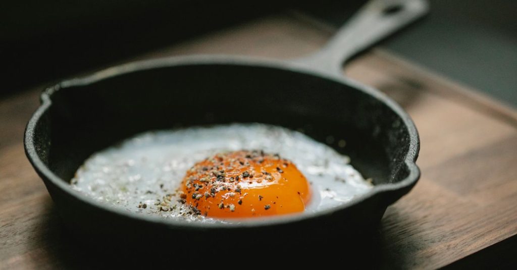 High angle of pan with fried egg with seasoning placed on wooden board in kitchen