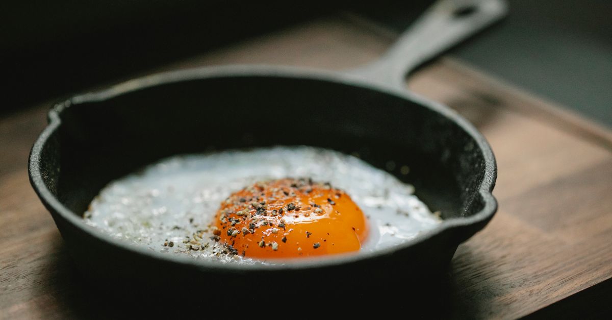 High angle of pan with fried egg with seasoning placed on wooden board in kitchen