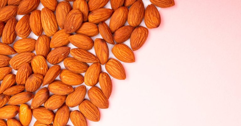 Organic almonds arranged on a pastel pink surface, perfect for health and nutrition themes.