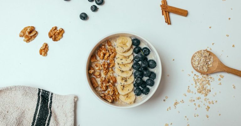A delicious and healthy breakfast bowl topped with bananas, blueberries, and walnuts on a white surface.