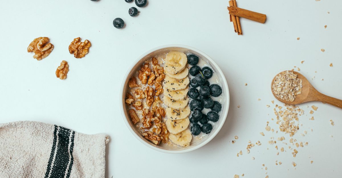 A delicious and healthy breakfast bowl topped with bananas, blueberries, and walnuts on a white surface.