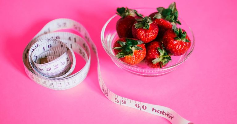 A glass bowl of fresh strawberries paired with a pink measuring tape symbolizes healthy eating.