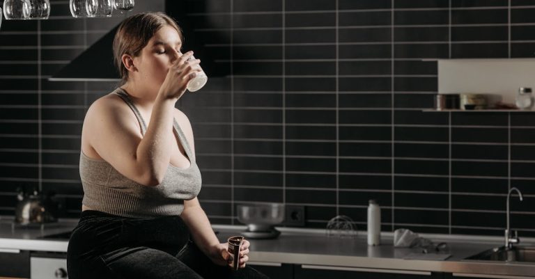 Woman sitting on kitchen counter drinking milk in a modern setting.