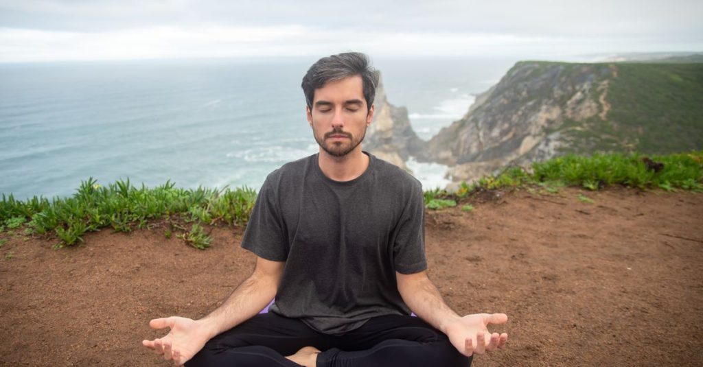 A man meditates on a cliff in Portugal, embracing calmness and nature.