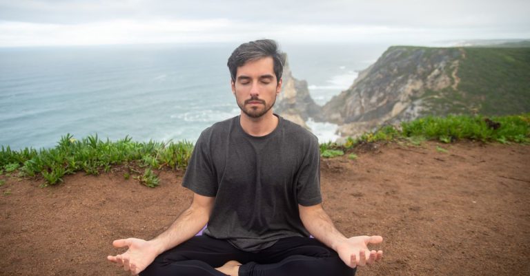 A man meditates on a cliff in Portugal, embracing calmness and nature.