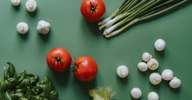 Flat lay of fresh vegetables including tomatoes, mushrooms, and spring onions on a green surface.