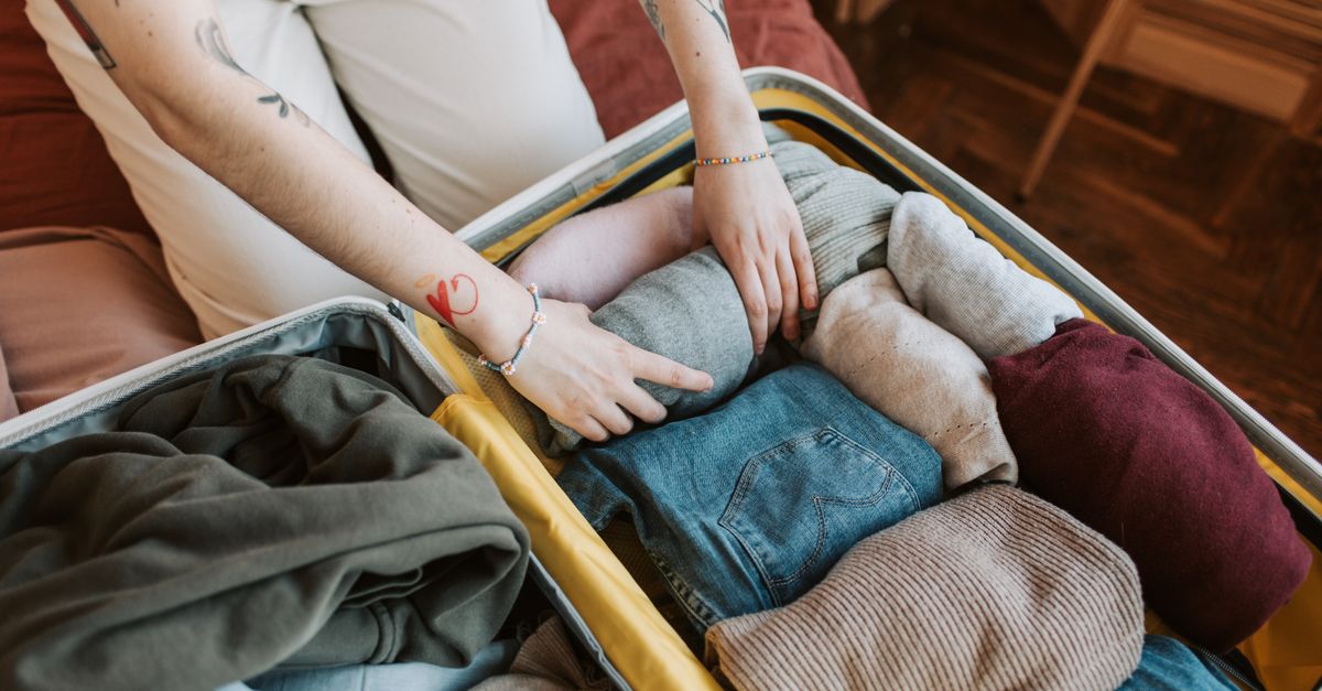 Close-up of a person packing various clothing items into a suitcase, ready for travel.