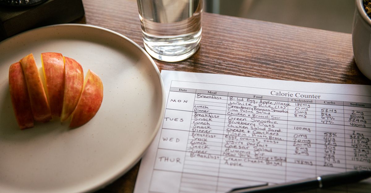 A table setup with apple slices, a calorie counting sheet, and a glass of water for a dieting scene.