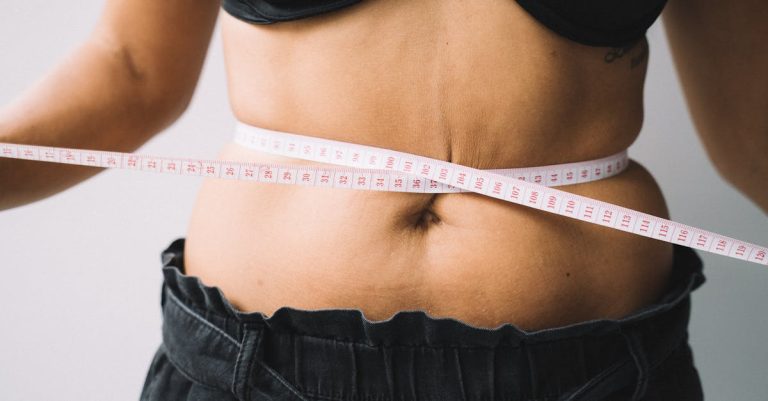 A person measuring their waist with a tape, symbolizing fitness and health goals.