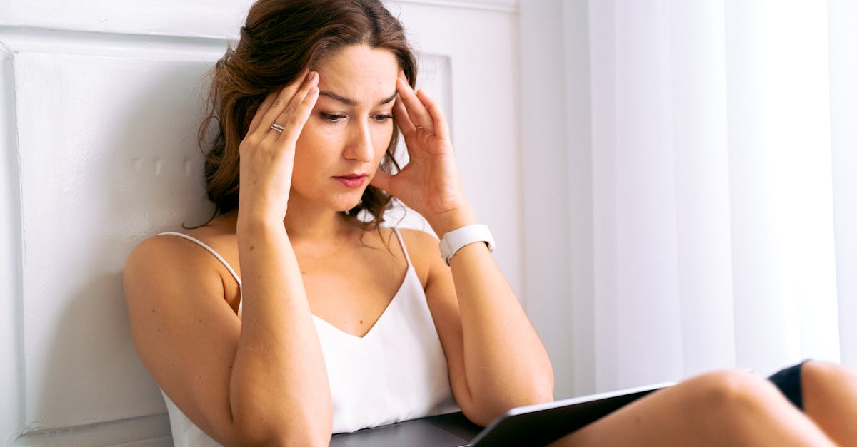 Young woman sitting with hands on head, looking stressed while working on a laptop indoors.