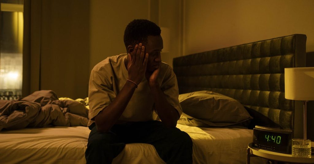 African American man sitting on a bed struggling with insomnia at night.
