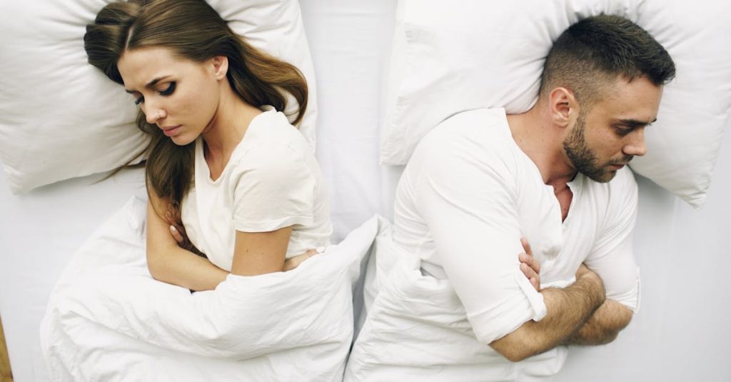 A couple lying in bed facing away, expressions of discontent.