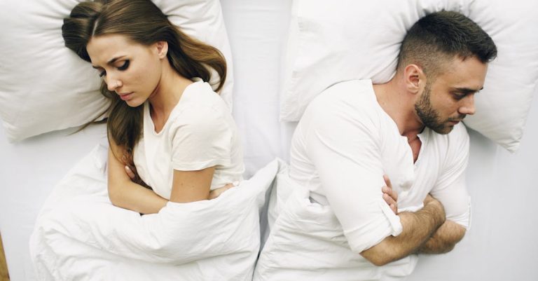 A couple lying in bed facing away, expressions of discontent.